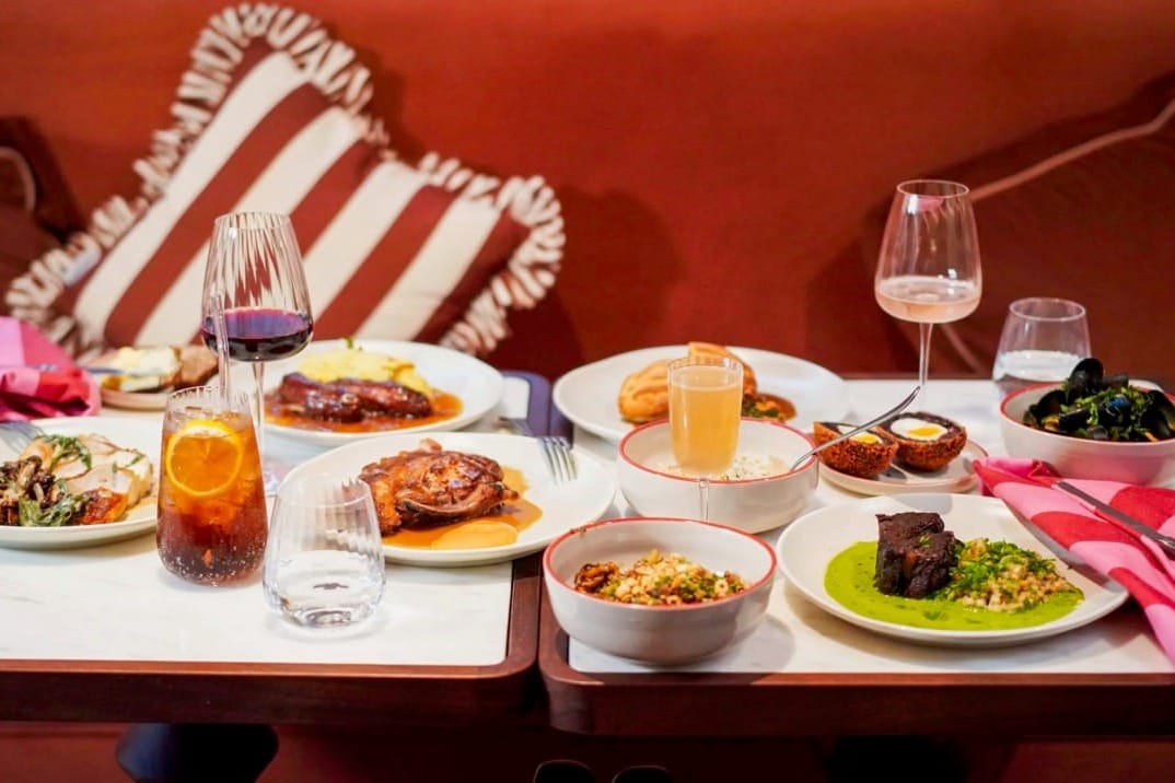 Two restaurant tables with many dishes and glasses of food and drink on it