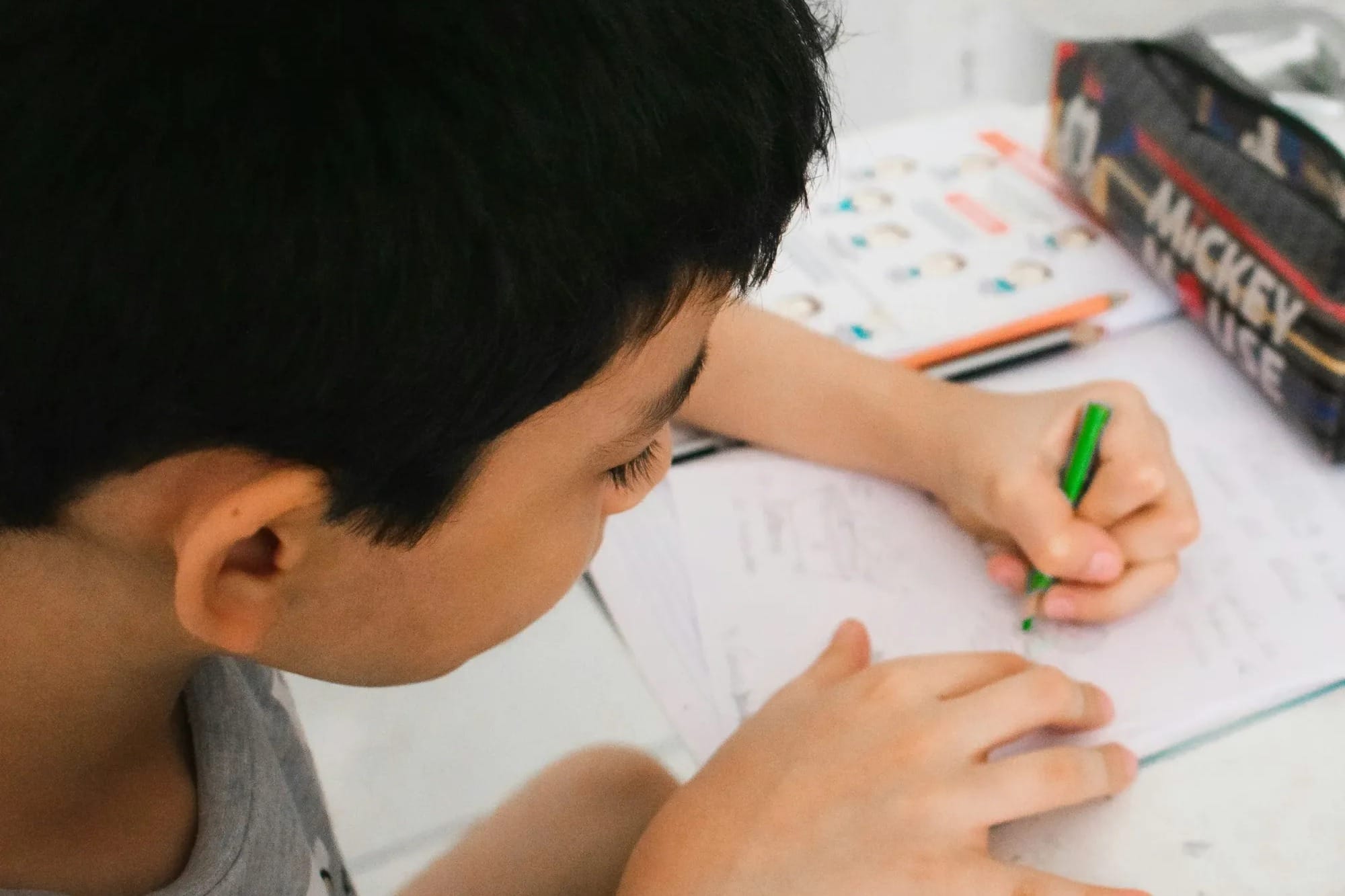 Close up of boy writing with his left hand at his desk