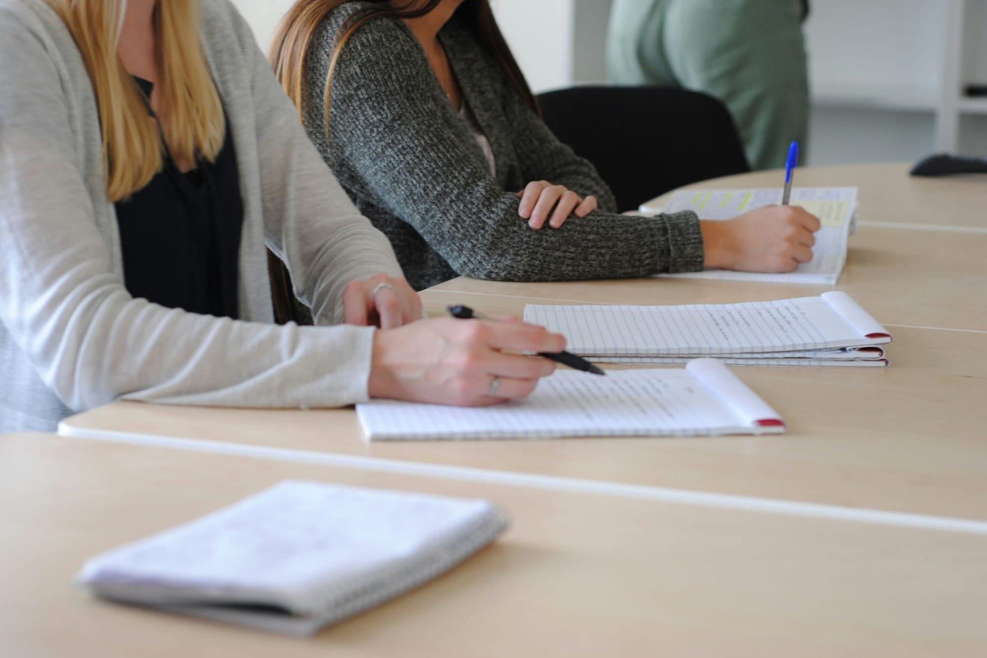 Close up of two women wearing cardigans writing something on pads of paper