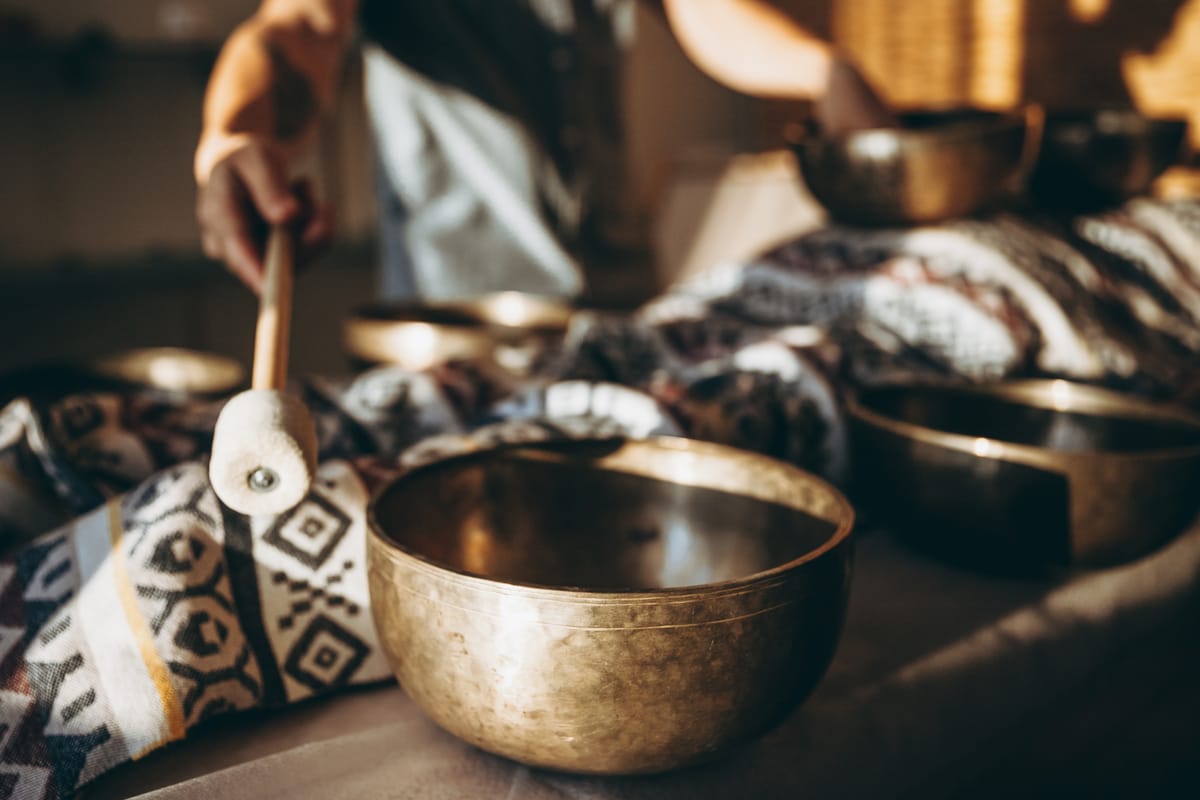 A person plays a metal bowl with a felted beater