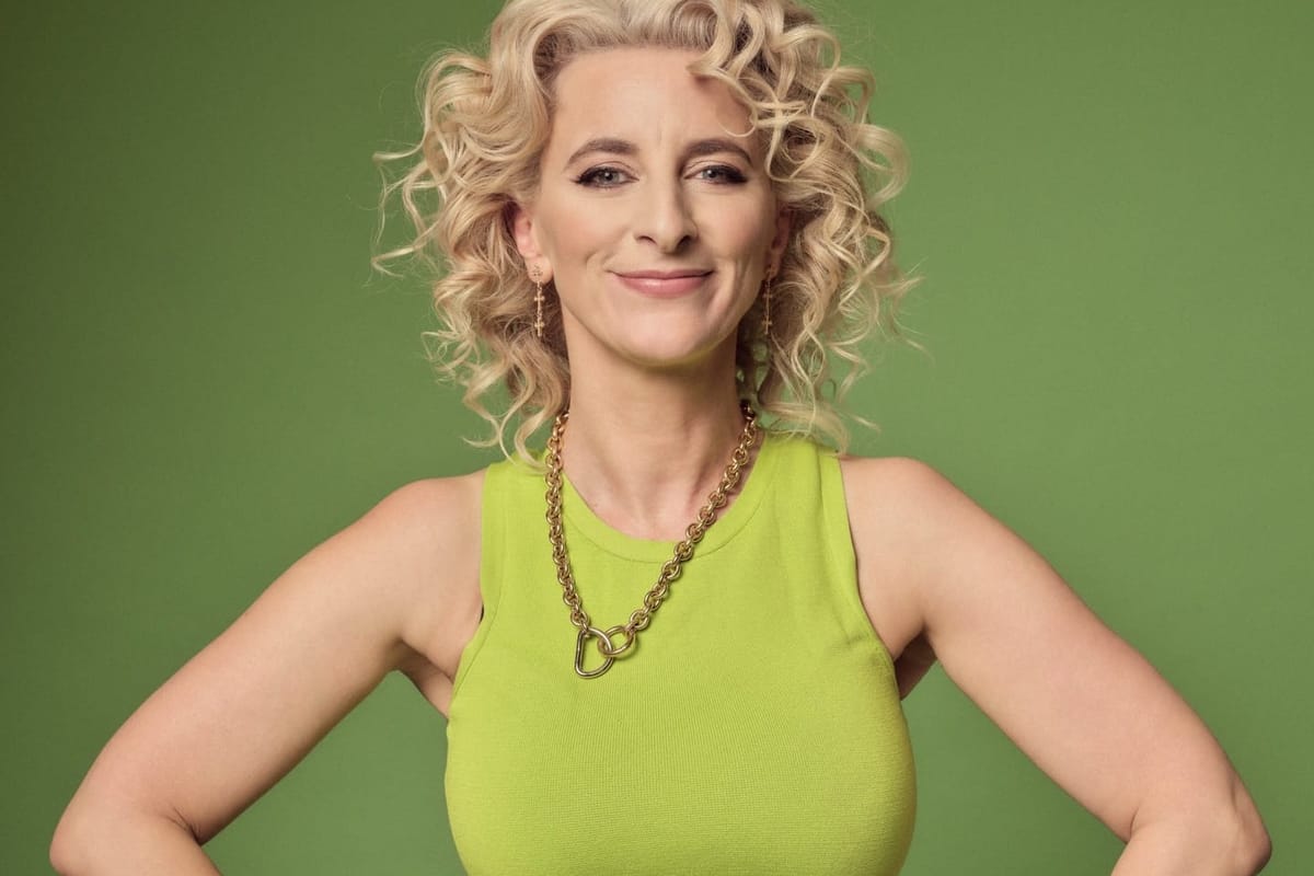 A blonde women in a green vest stands against a green background