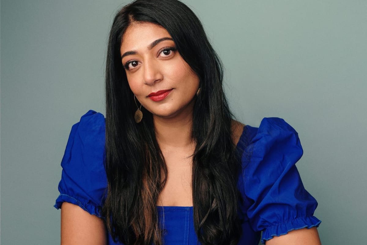 A woman in a blue dress looks directly into the camera