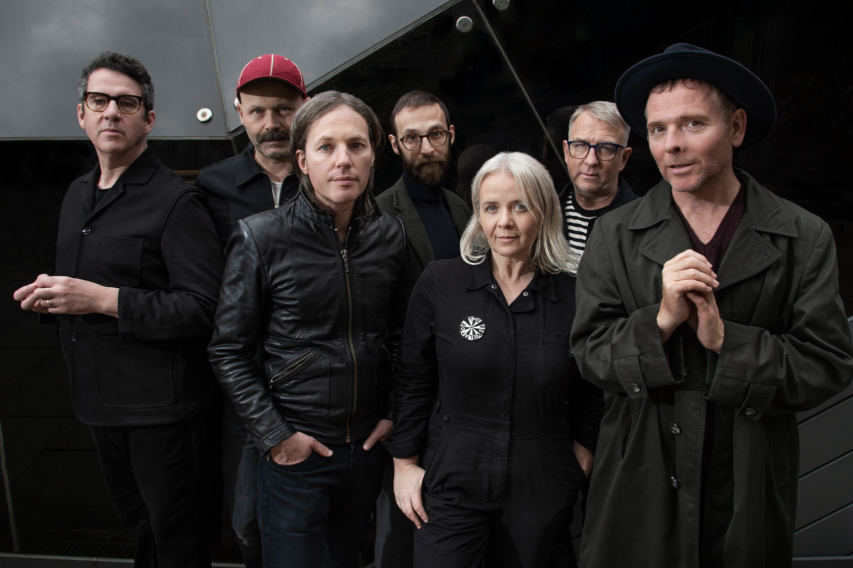 Seven people dressed in black. One wears a red hat. 