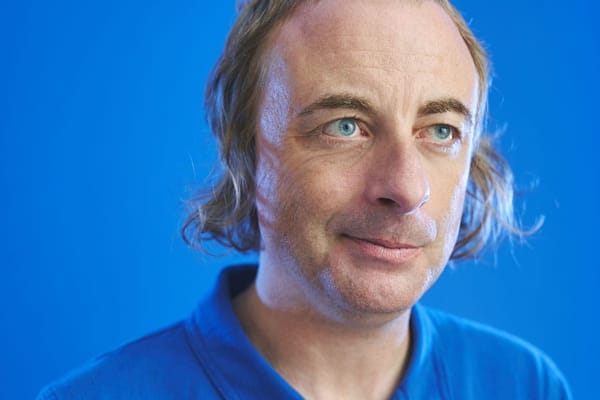 A man in a blue shirt stands against a blue background