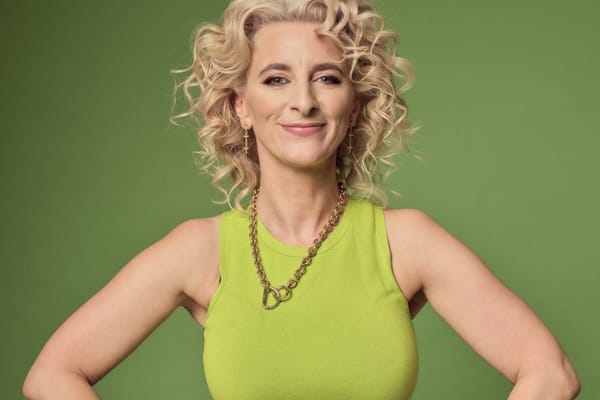 A blonde women in a green vest stands against a green background