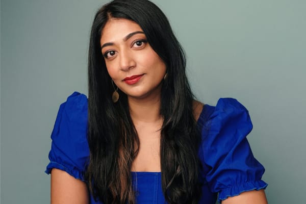 A woman in a blue dress looks directly into the camera